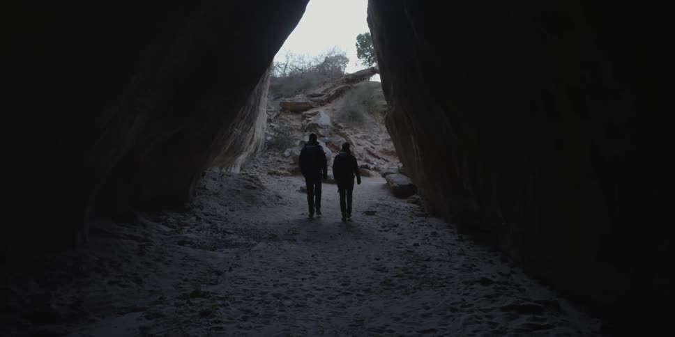 Two people walk outside of a dark cave together