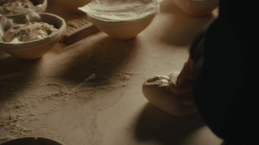 Close up of the hands of a baker kneading loafs of bread over a table on a rustic setting
