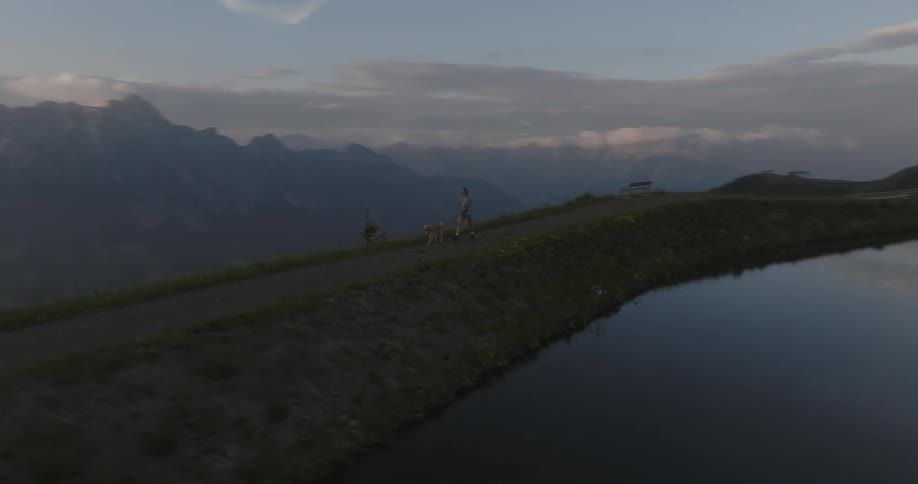Woman walking her dog on a narrow road on a mountain peak next to a lake