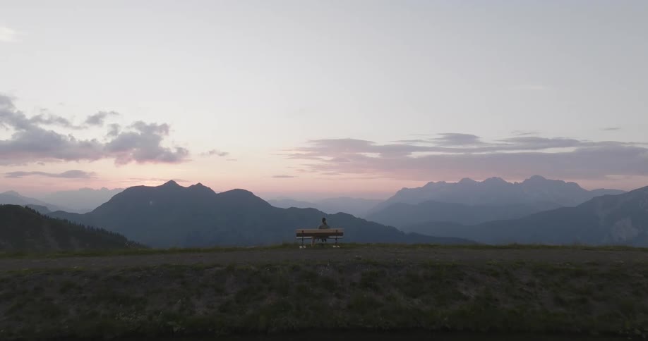 A person sitting on a bench behind a lake and in front there is a mountain range