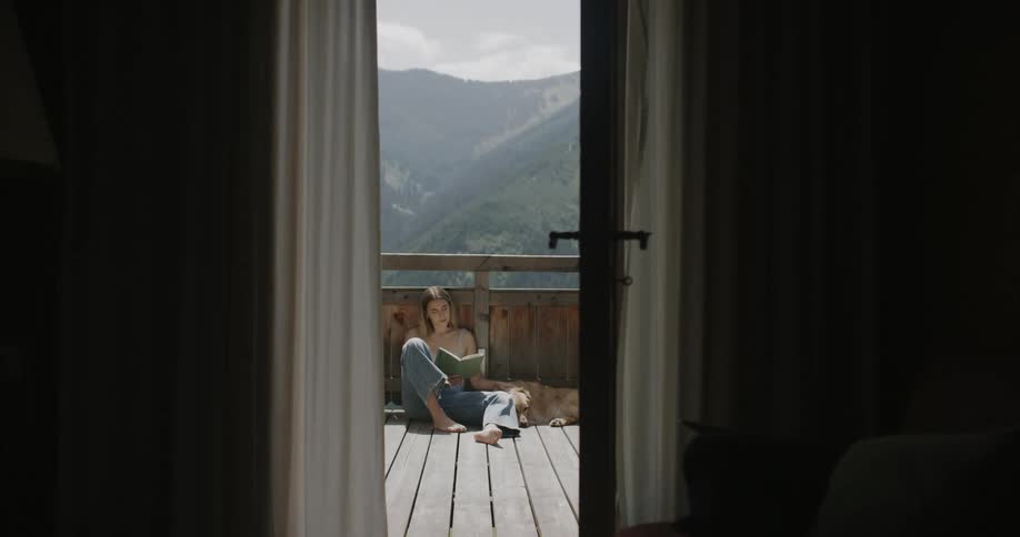 Woman sitting on a porch reading a book and a golden retriever beside her