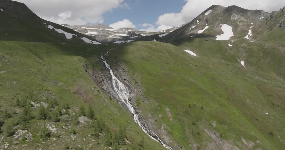 A waterfall cascades down a hill in a mountain range on a mostly cloudy day