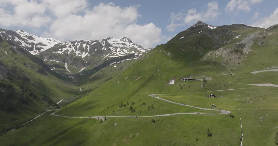 Aerial panorama of a winding street with greenish mountains and snowcapped peaks