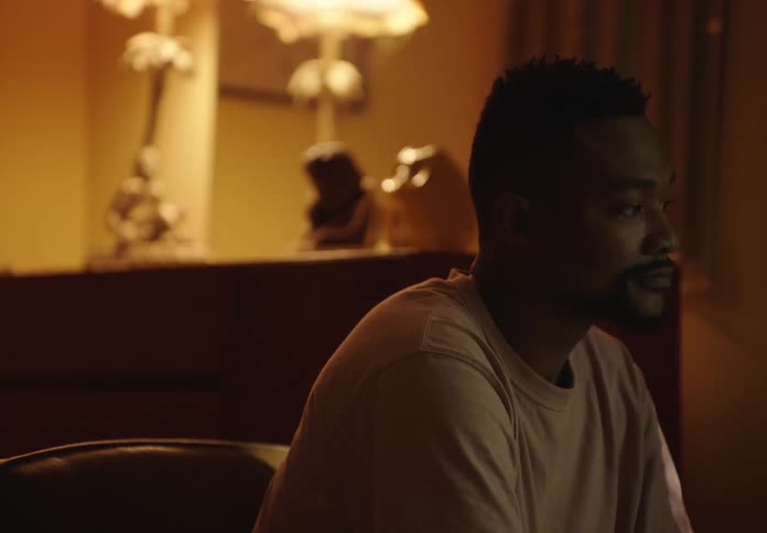 A man in a living room sitting on a couch starts to talk