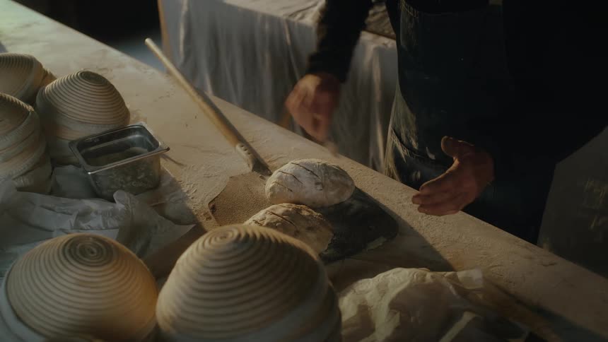 An adult scores two loaves of bread dough and picks them up on a pizza peel