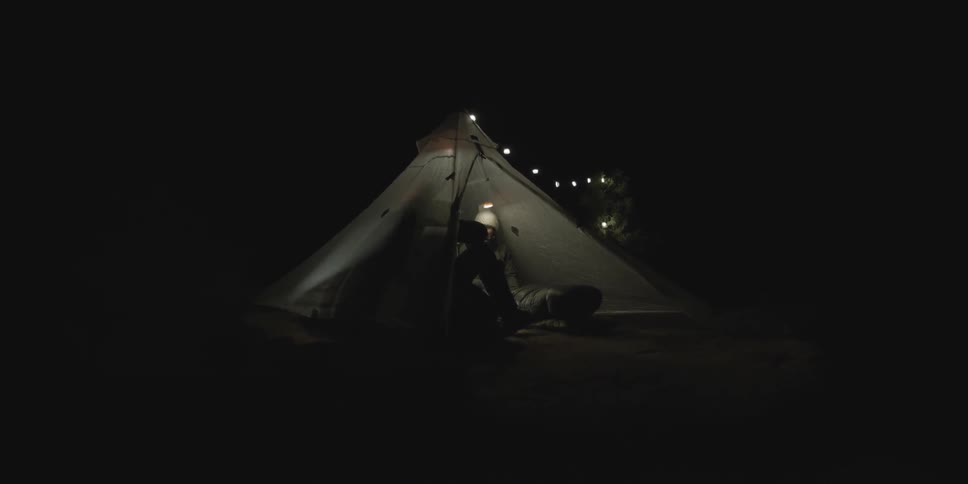 Man entering a small lighted tent that is already occupied by a woman