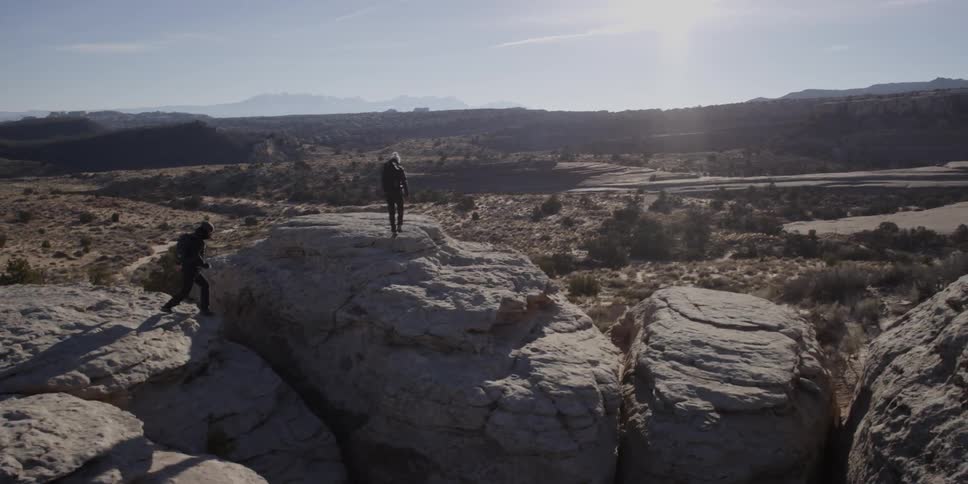 Two hikers leap across rocks cliffs