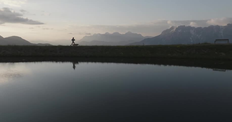 Landscape of a lake on a mountain peak and the silhouette of a woman running with a dog in the background