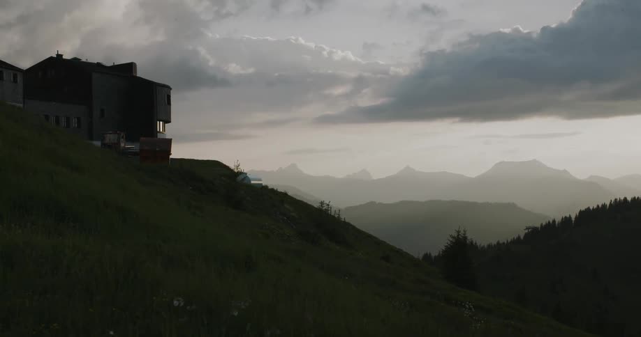 Modern architecture home on top of a green hillside with fog covered mountains in the background in the evening