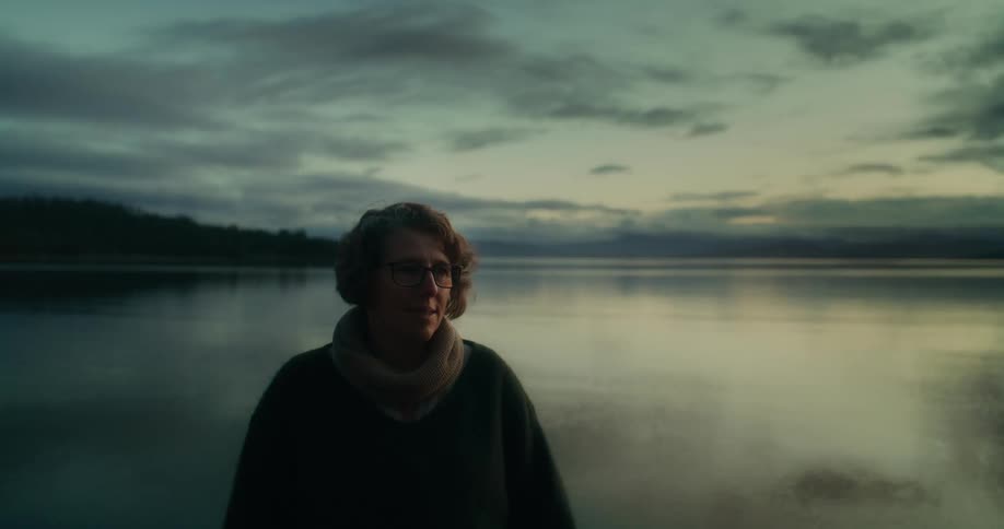 Woman in a natural landscape with a lake in the background that reflects the cloudy sky