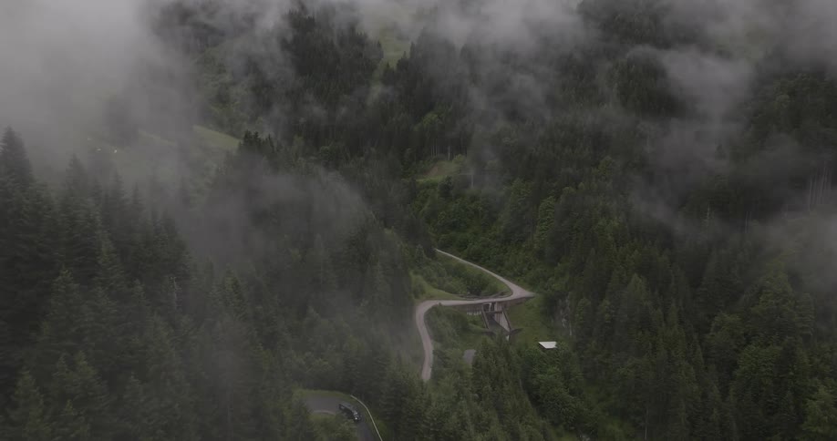 Mountain road bridge surrounded by dense forest and covered in clouds