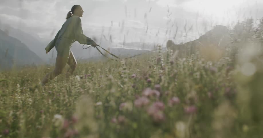 A woman and her dog walking through a field of wildflowers with distant mountains in the background