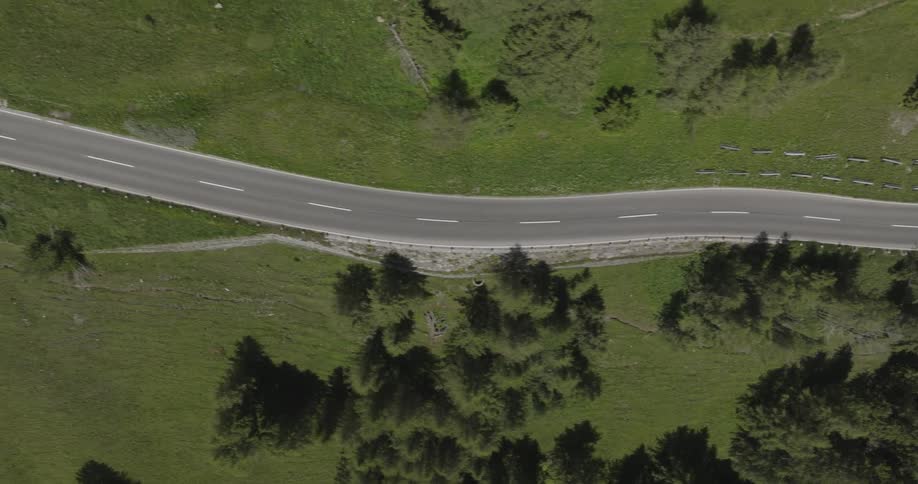 Aerial view of a twolane curved road surrounded by green areas with trees and grass