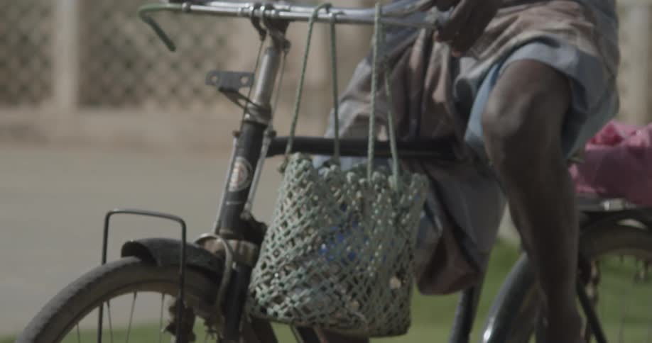 Close-up of a man riding a motorcycle with a green basket hanging from the handlebars