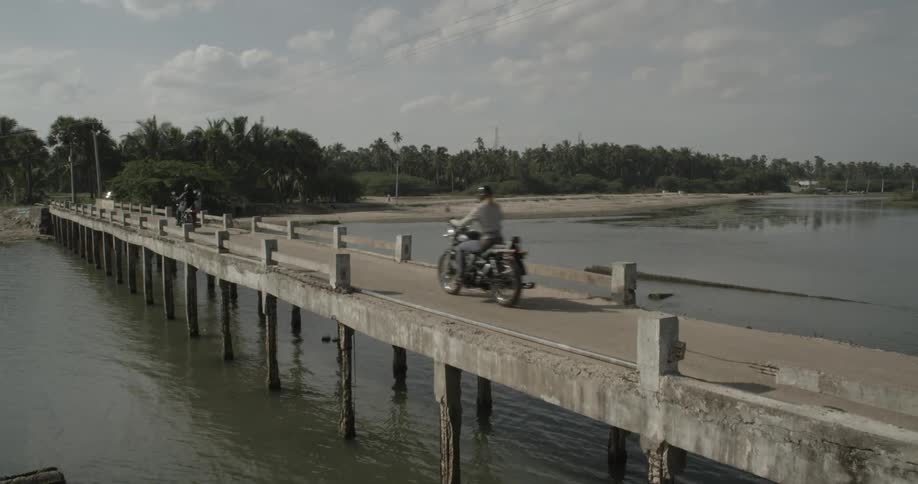 Two motorcycles drive across a narrow bridge