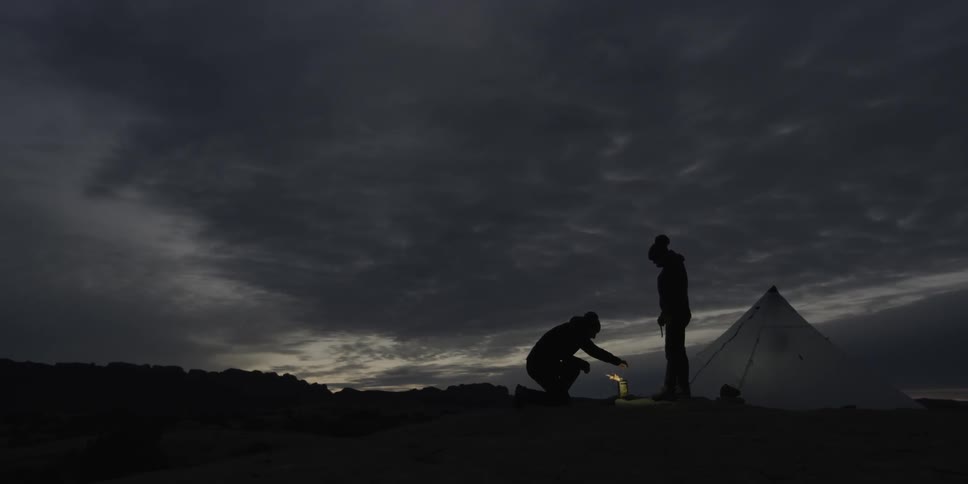 Two campers huddle around a small fire