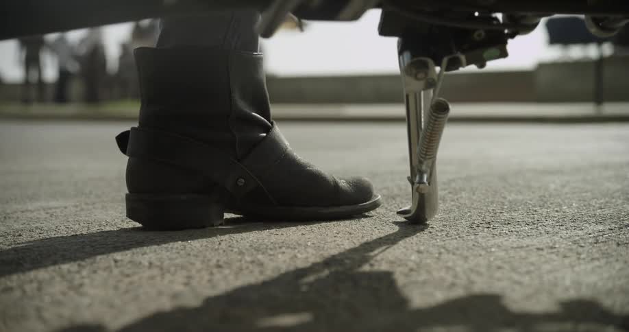 A person puts the kickstand down on their motorcycle