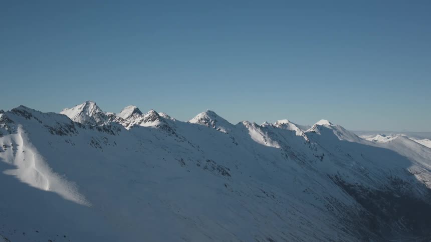 The sun shines on a large mountain range covered in deep snow