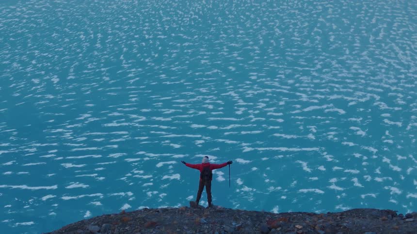 A hiker is standing at the peak of the mountain over the iced over lake