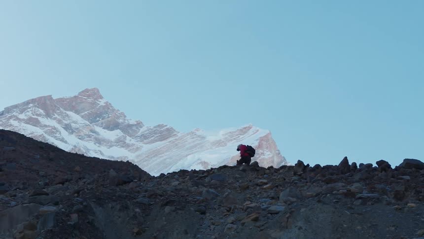 A hiker ascending a rocky terrain with snow capped mountains in the background