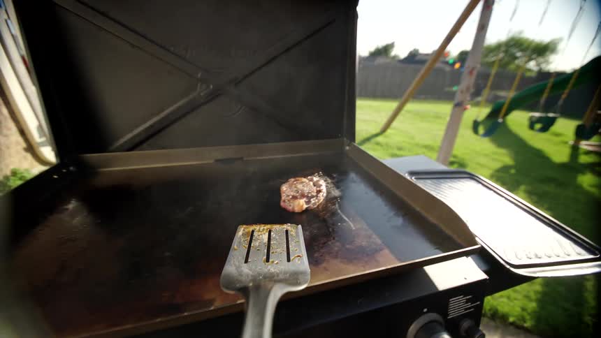 A spatula flips steak over on a grill in a backyard