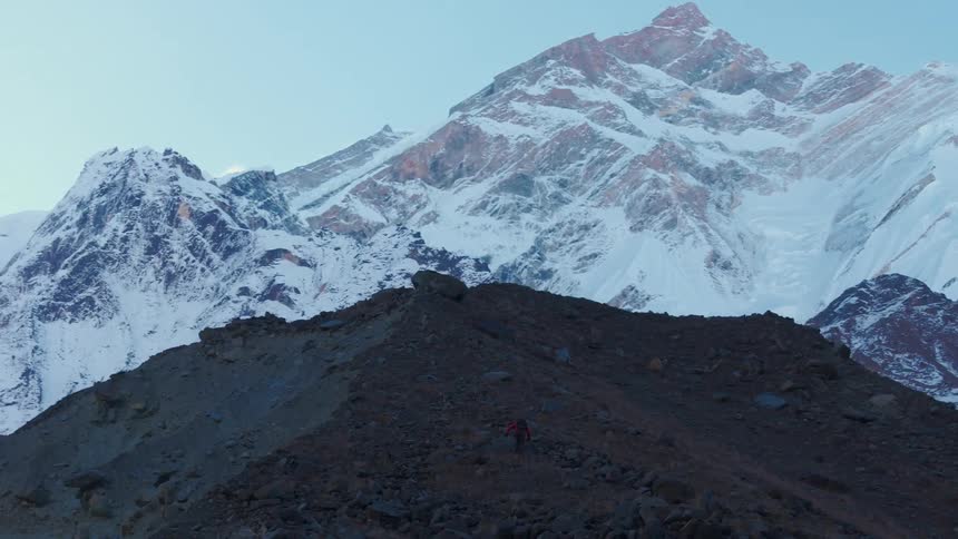A lone hiker makes their way up a steep slope towards a towering mountain