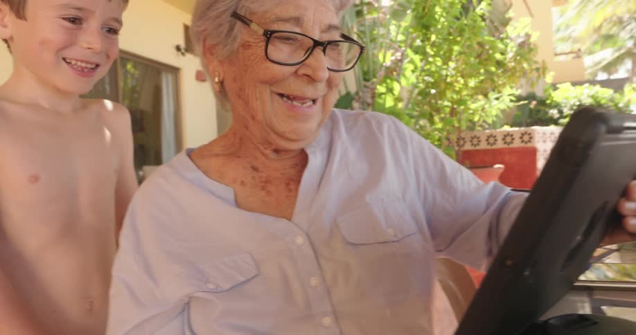 Grandmother and grandson look at a tablet while smiling and laughing