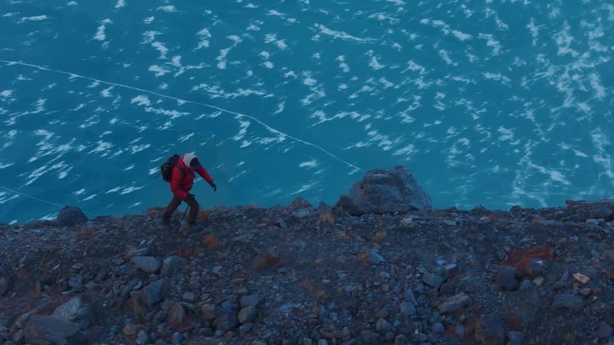 A person in red clothing hiking up a steep rocky slope overlooking a frozen body of water