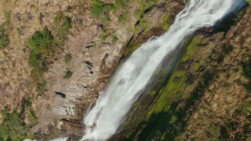 White water waterfall flowing over a rocky surface with areas of green vegetation