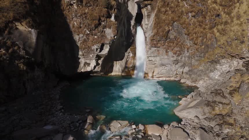 A serene waterfall cascading into a clear blue pool surrounded by rocky cliffs and lush vegetation