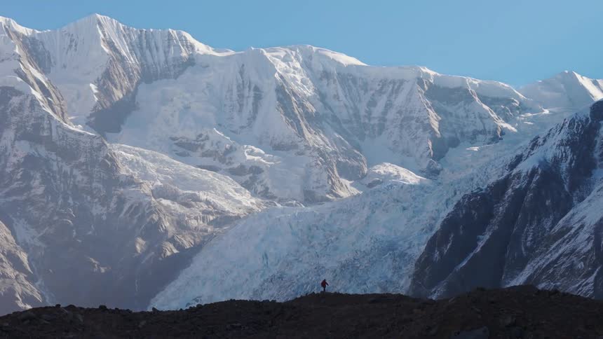 Person hiking across a summit surrounded by snow capped mountains in the background