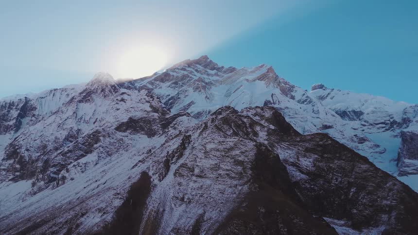 A range of mountains that are partially covered in snow in contrast to the clear blue sky