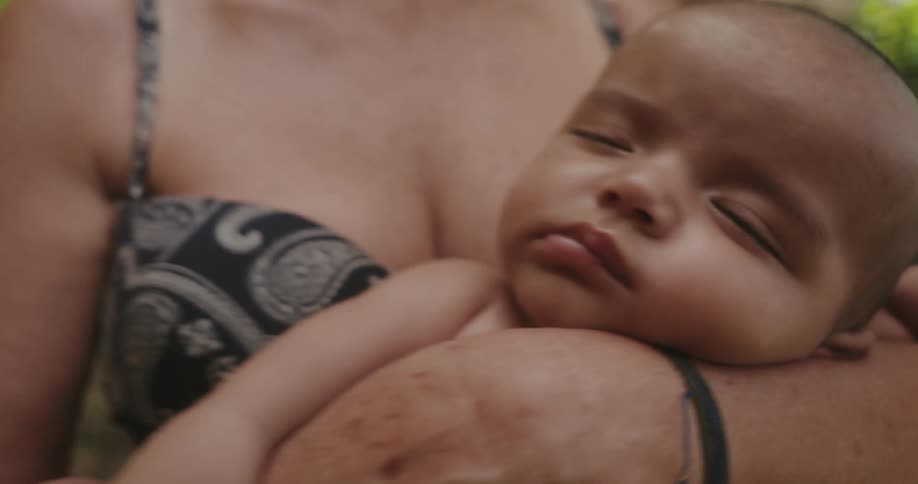 A mother is holding her baby while swaying back and forththe baby only has his eyes open for a second before going to sleep