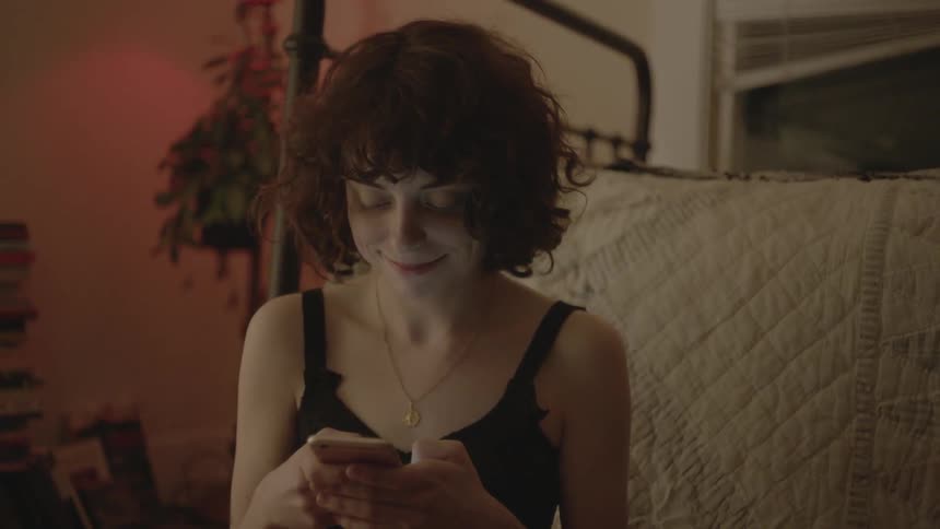 A woman smiles while looking at her phone on the floor of a bedroom