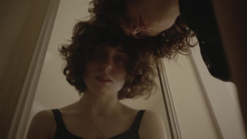 Curly haired woman leaning forward and touching her head against the mirror while looking sad