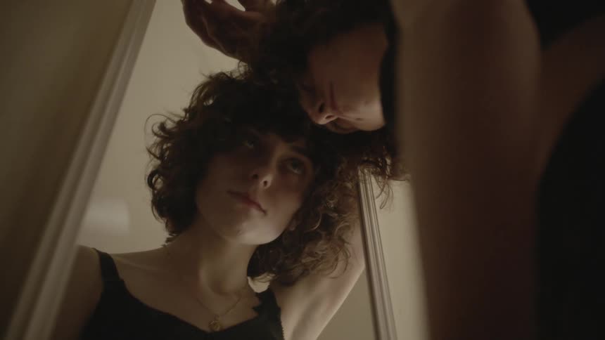 A woman rests her head against her bedroom mirror