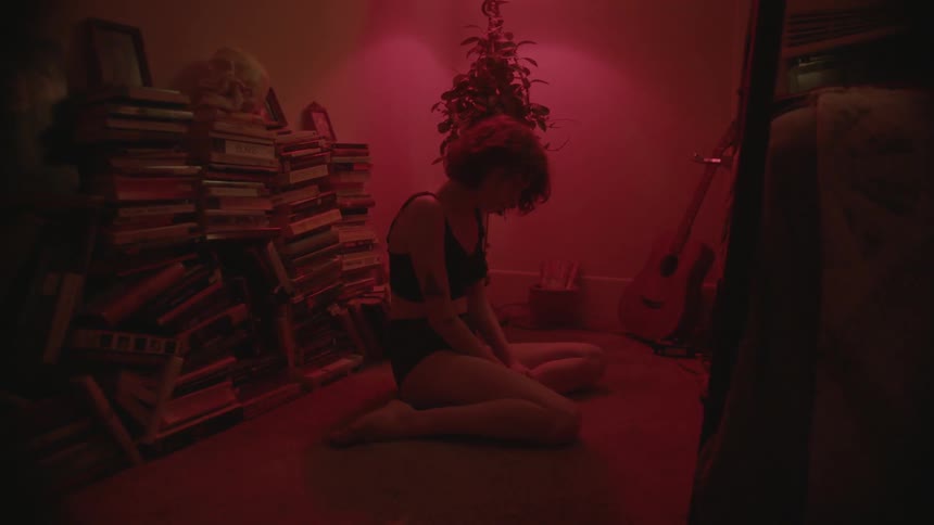 A woman is sitting on her knees in a room with a red light