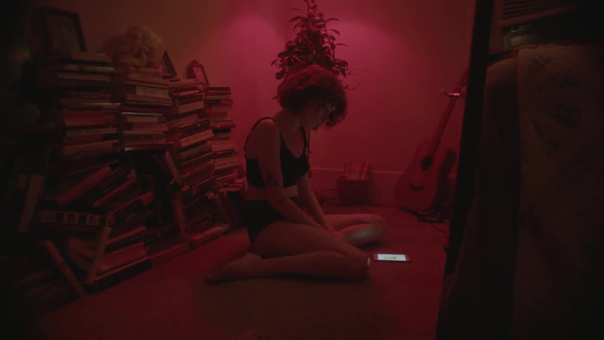 A woman sitting on her knees in a red lit rood is looking at her phone