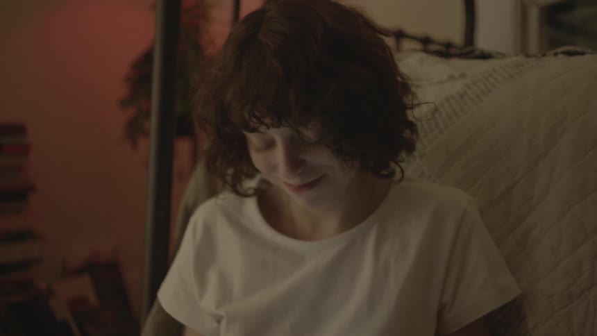 A woman is sitting in bed smiling as she reads something