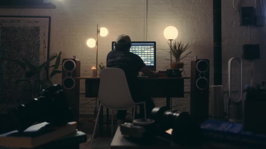 Man in a dimly lit room sitting in front of his computer in a studio