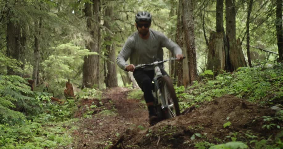 Man riding at high speed whips his mountain bike off of a jump on the forest trail