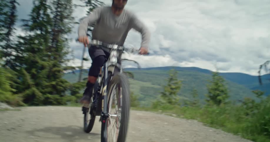 A male mountain bike rider pedals past the camera on a dirt road ascent up a mountain