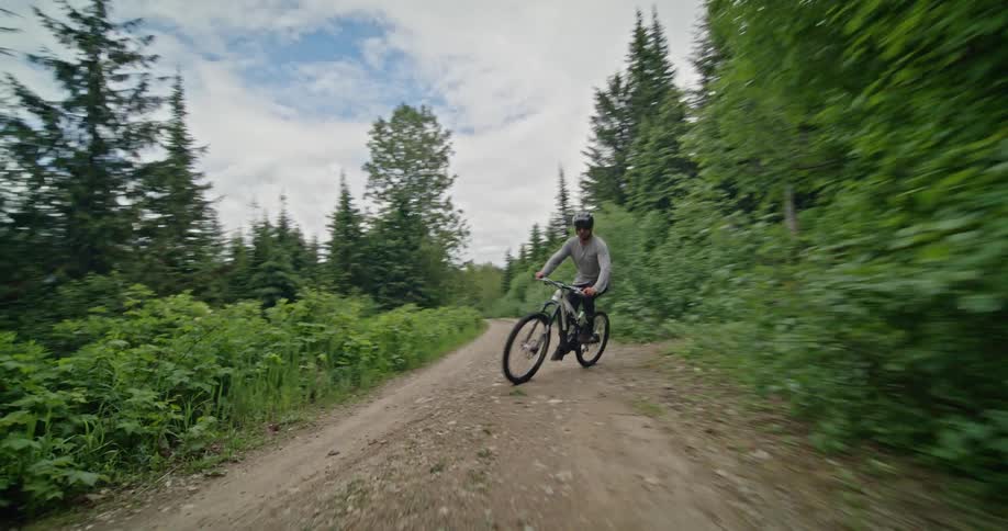 Person riding a mountain bike exits a forest trail onto the gravel road