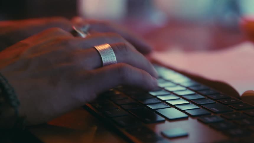 A man wearing rings types rapidly on a computer keyboard