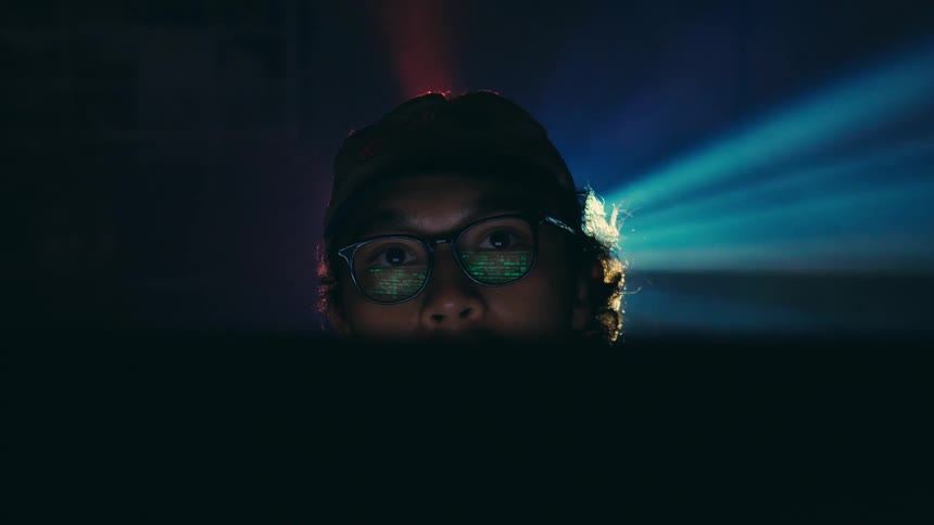 Portrait of a man wearing glasses and a cap in a room with reflective lights in the background