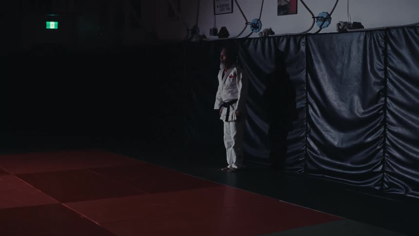 Older male martial artist bows while facing the martial arts competition floor