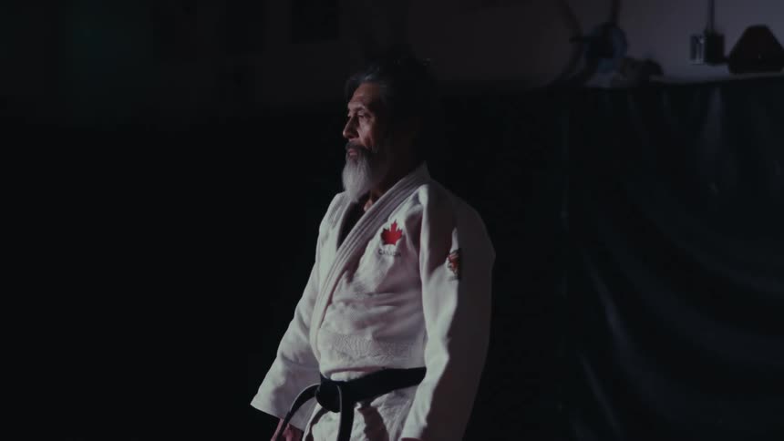Martial artist wearing a gi and black belt standing still in the darkness