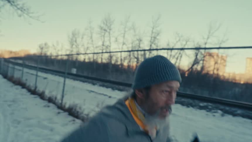 An older man is running on a snowy path with bare trees in the background