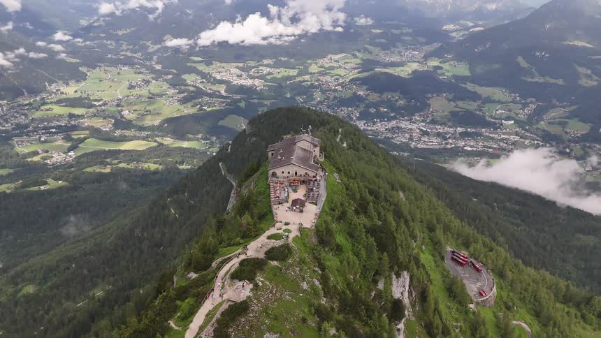 Tourists visit a large building on the top of a heavily forested mountain