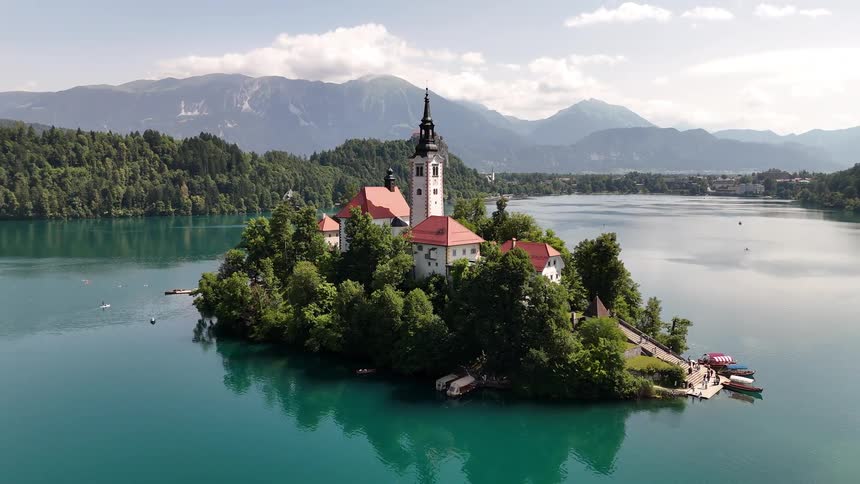 An island with a big house with a tower in the middle and around the blue water of a lake with forest on the banks